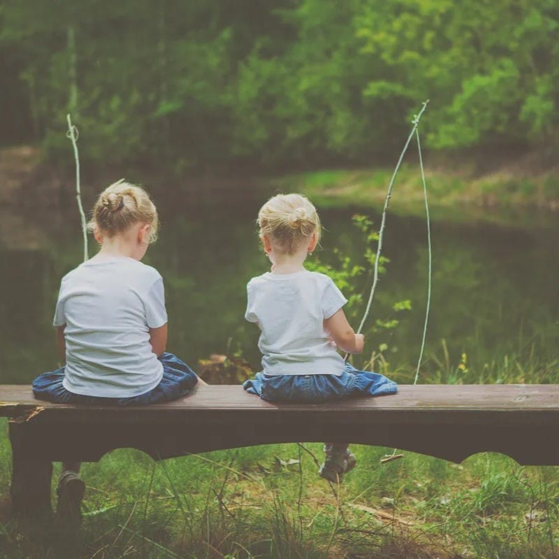 Two little kids fishing while sitting on bench.
