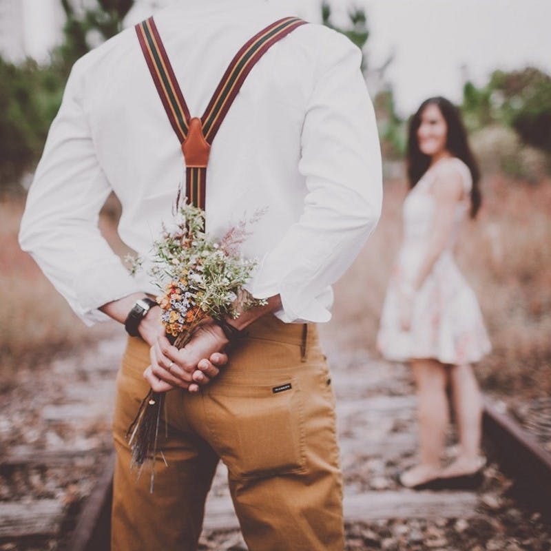 Man standing in front of women hiding flowers behind his back.