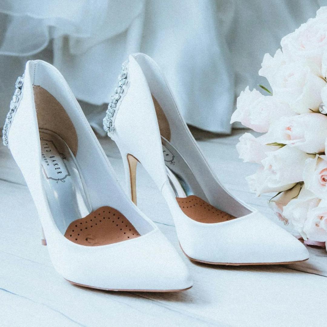 Wedding shoes on ground with bouquet of flowers.