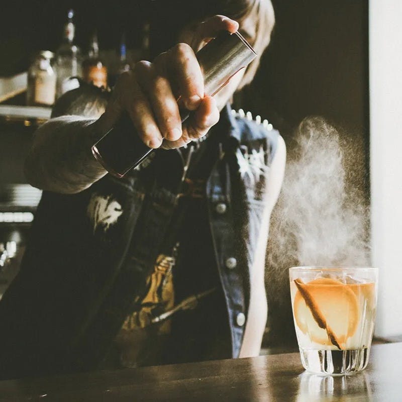 Man spraying mist on cocktail drink.
