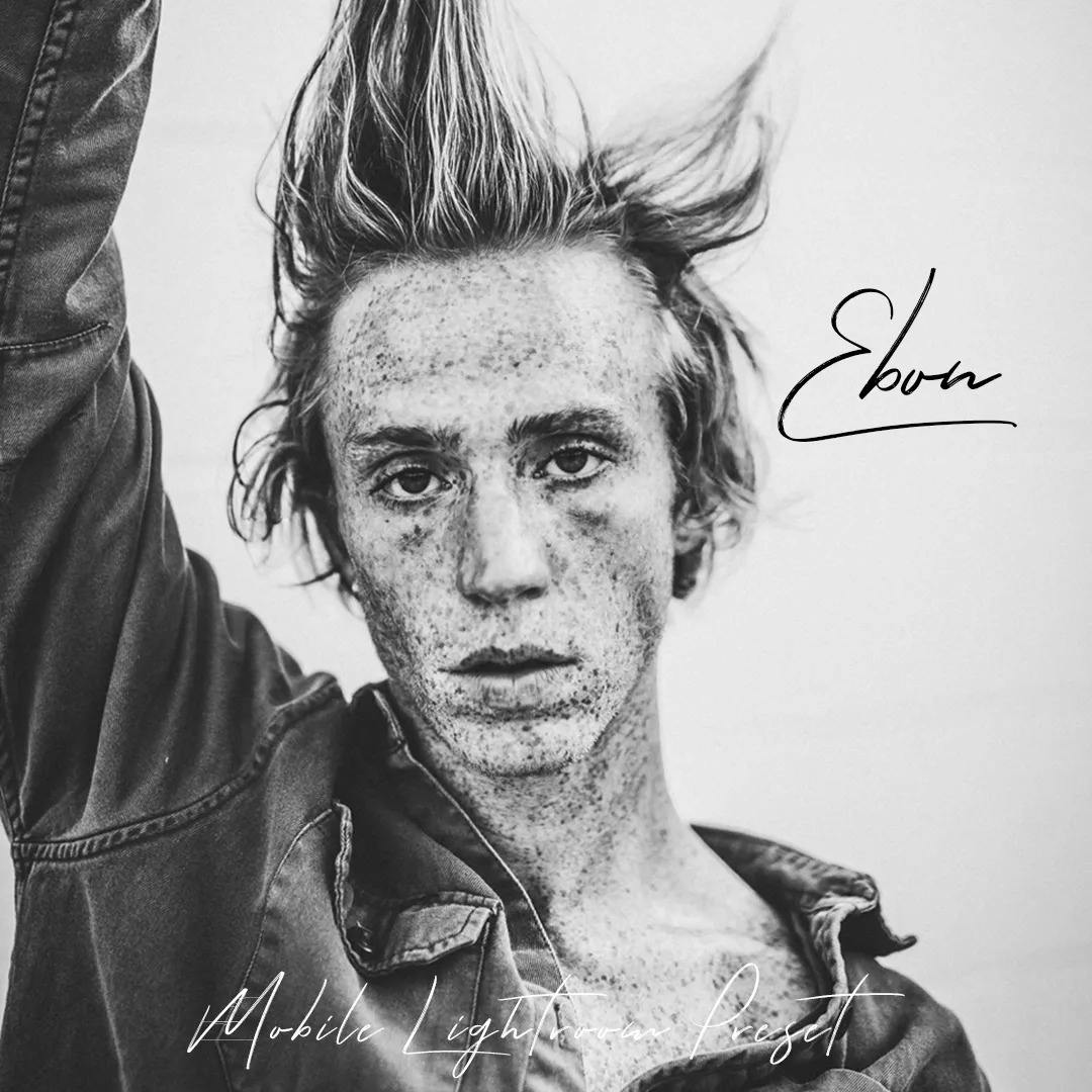 Freckled guy holding his hair up with one hand in black and white.