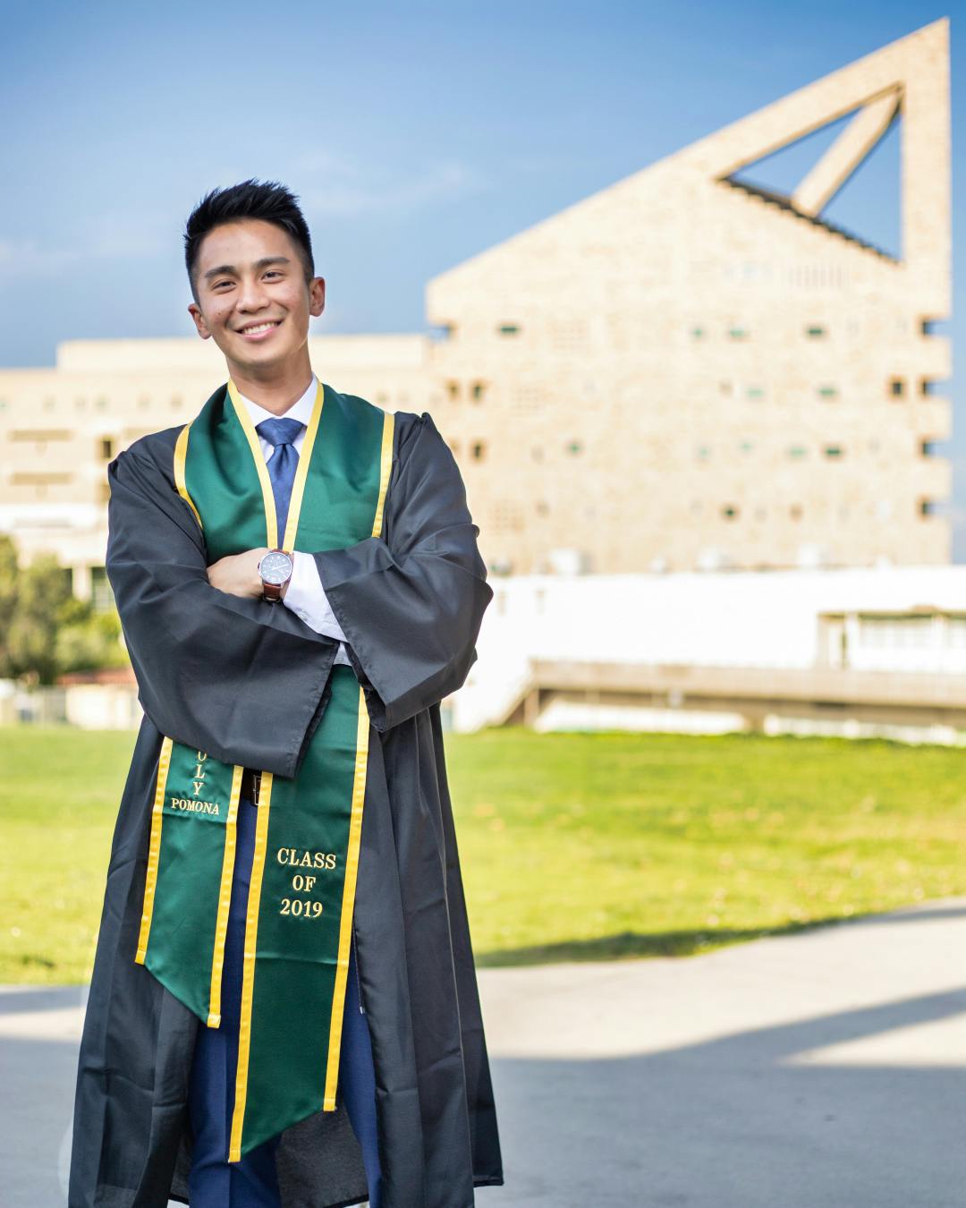Man standing in graduation gown next to building.