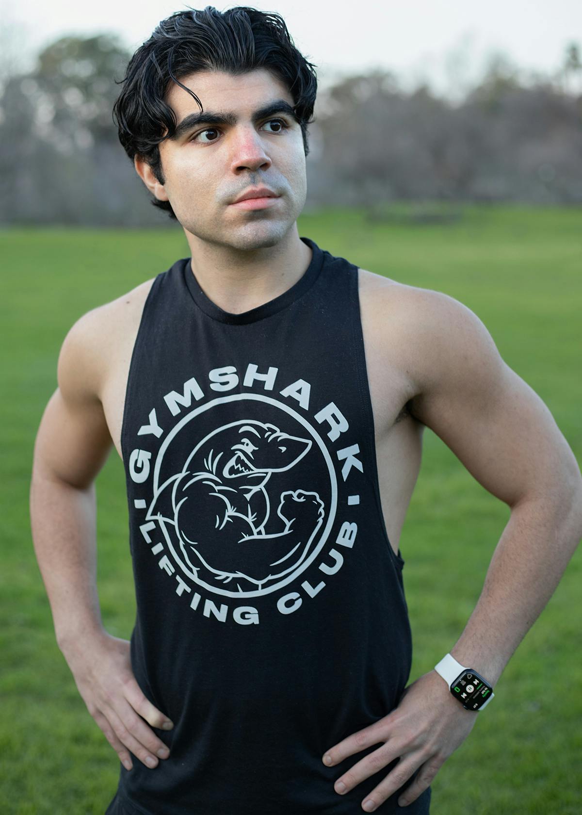Man posing in park wearing Gymshark tank top during cloudy ambient light.