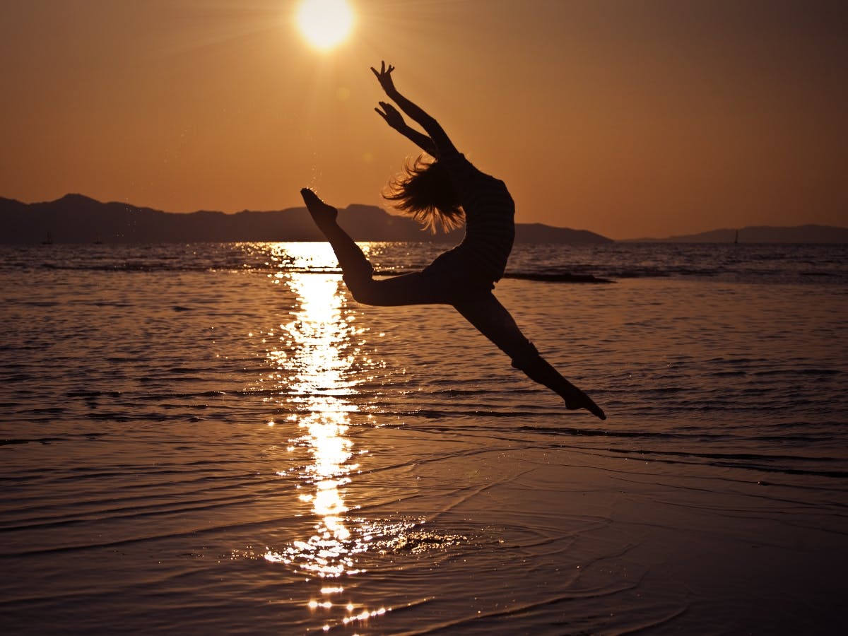 Woman hitting dancing pose on beach creating a silhouette.