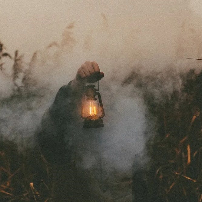 Man holding lamp in field with smoke.