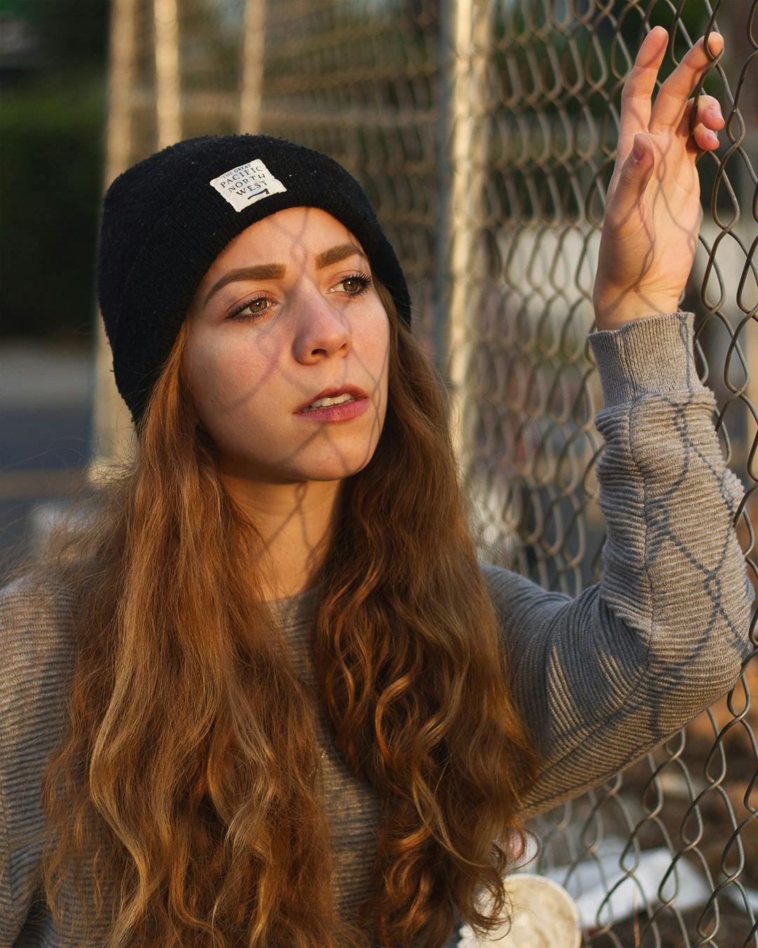Girl in beanie against fence during golden hour.