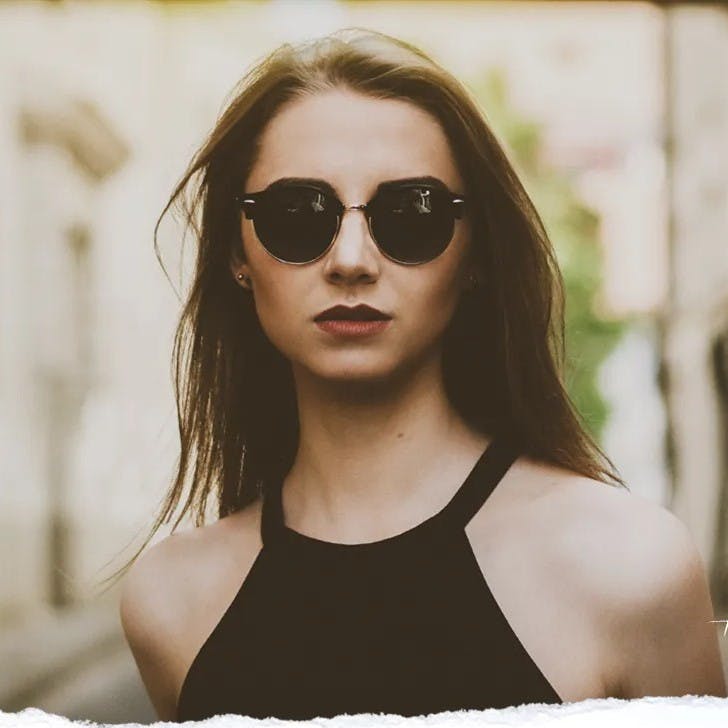 Woman with sunglasses and black outfit looking at camera.