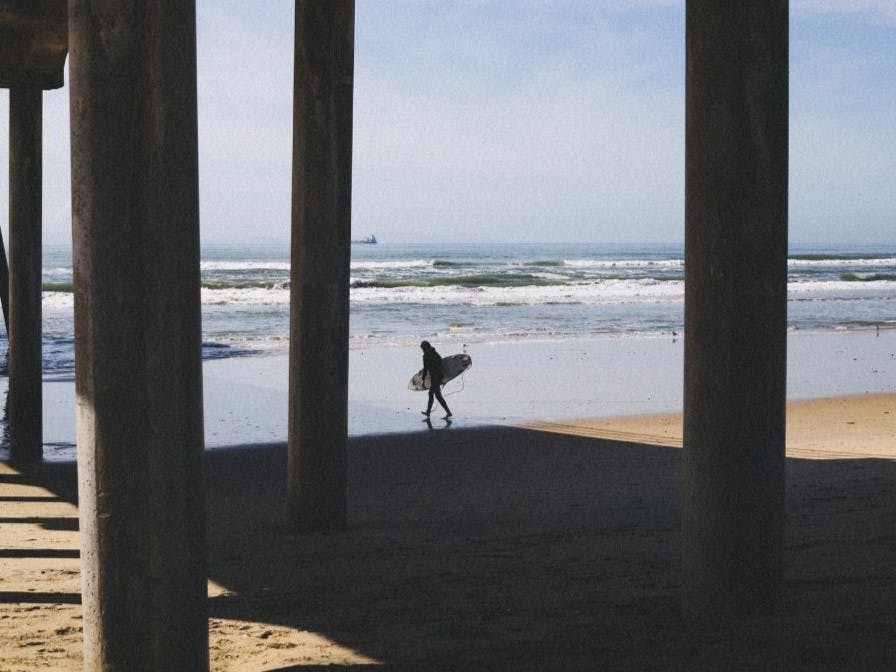 Surfer walking between two pier columns.