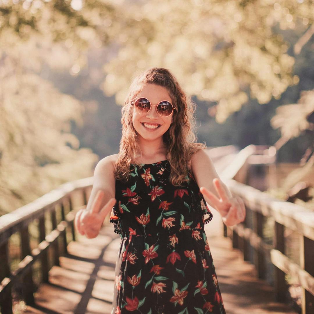 Girl giving peace sign while standing on bridge.