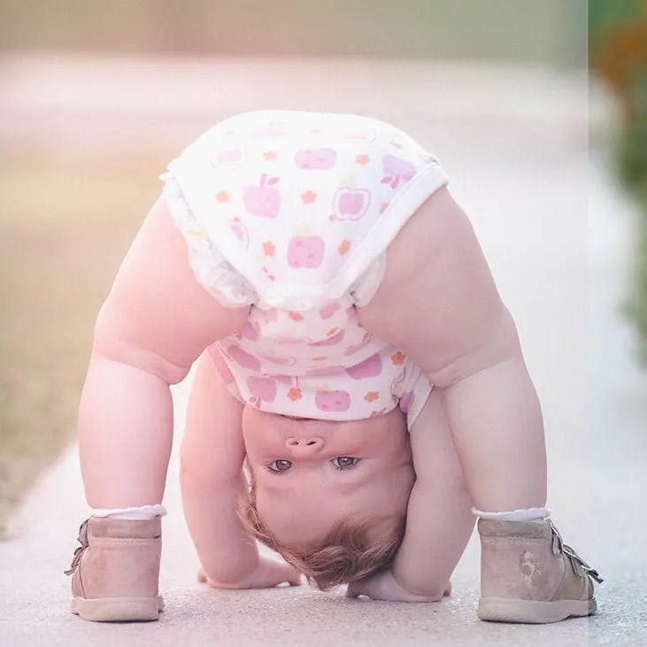 Baby looking through legs with hands on ground.