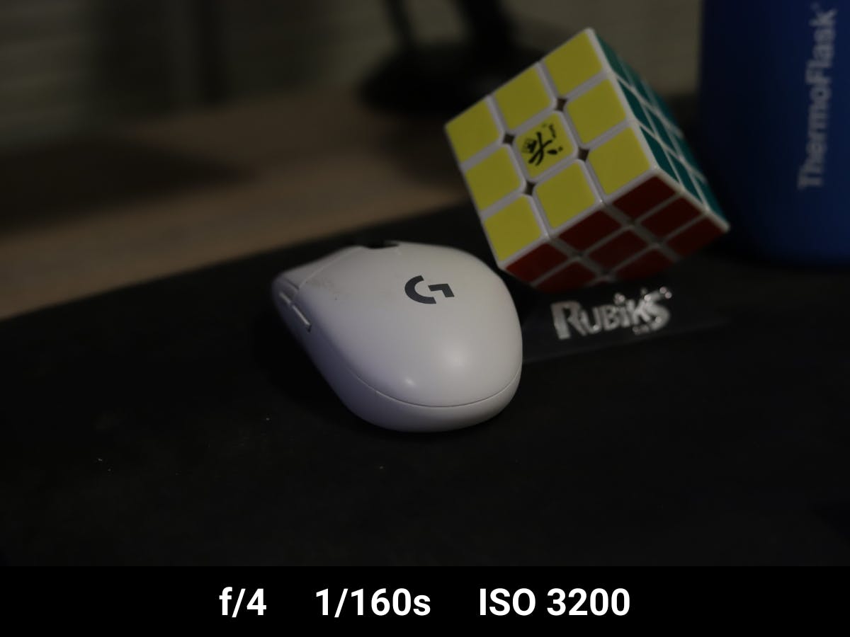 Mouse on a desk next to Rubik's cube in underexposed photo.
