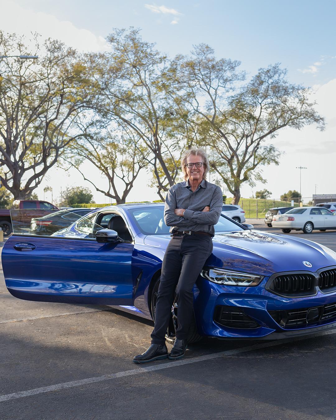 Man leaning against his new blue car.