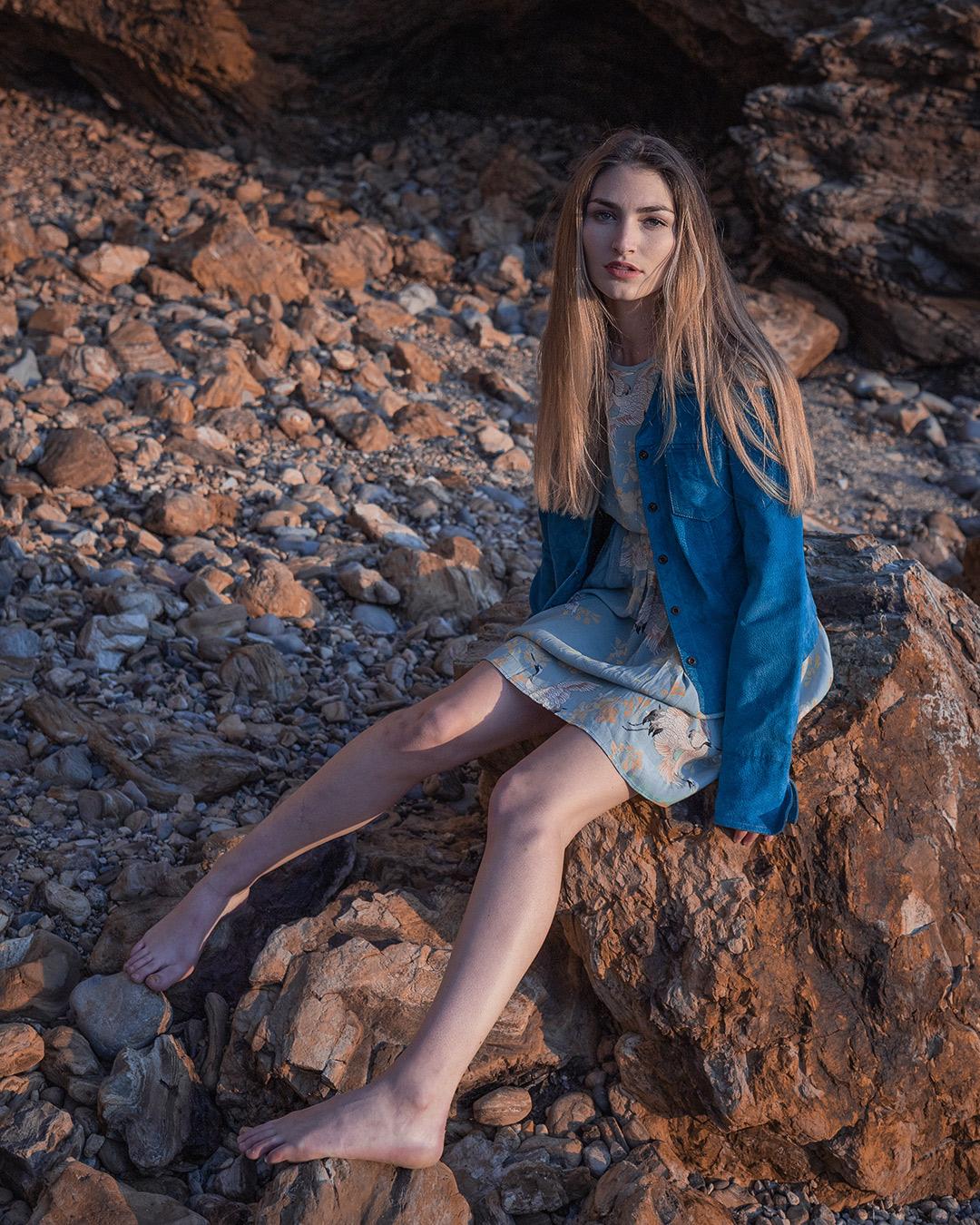 Woman sitting on rock both legs spread.