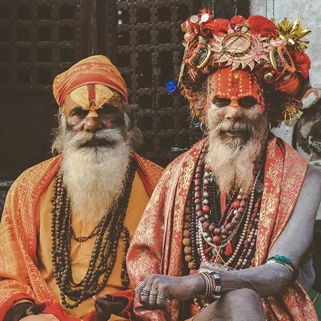 Two men sitting down wearing orange traditional headgear.