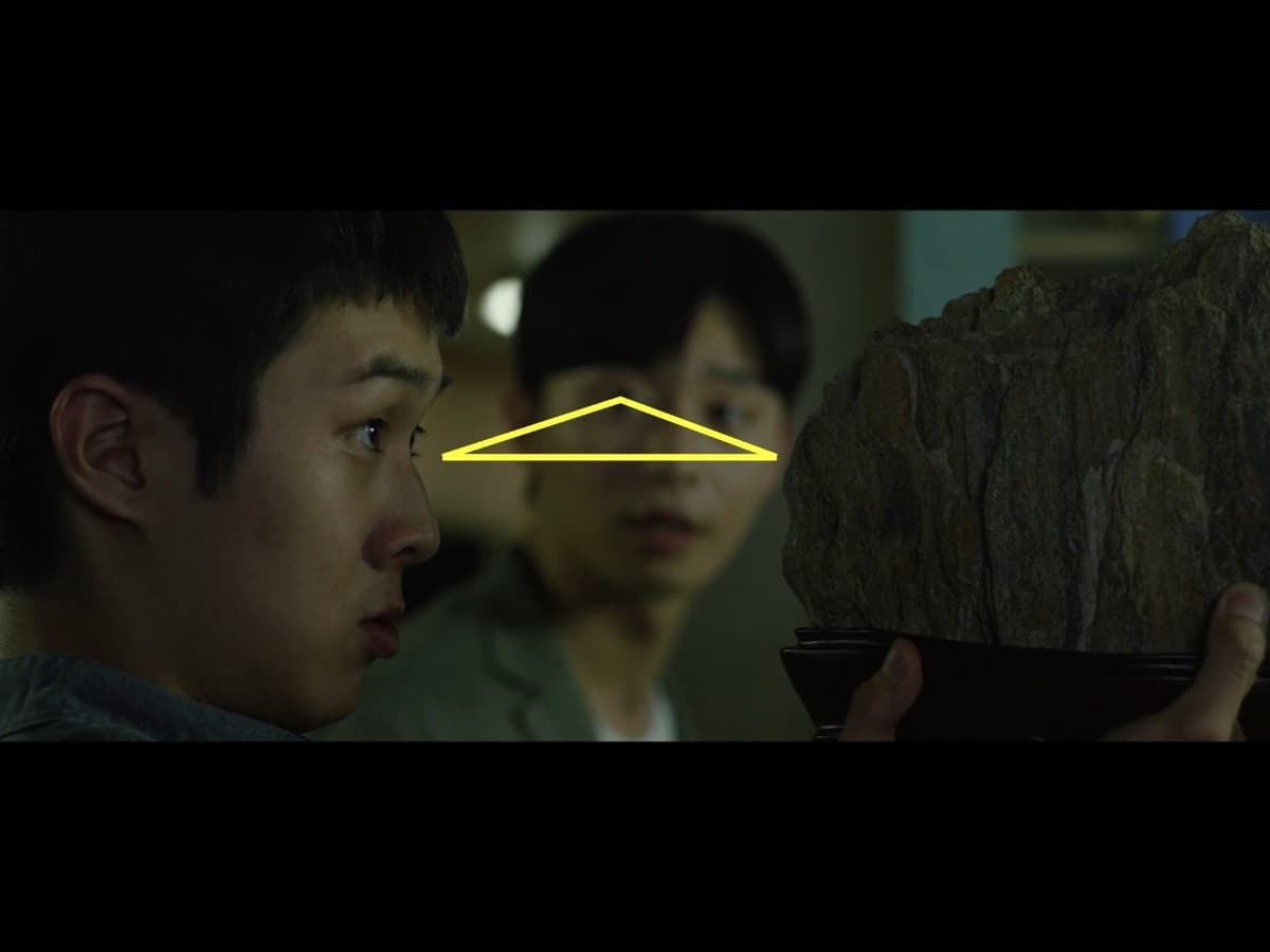 Parasite scene 3 - visual triangle Composition from scene from Parasite where Ki-Woo is gifted scholar's rock.