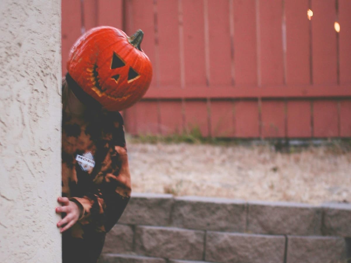 Pumpkin head photoshoot example Person peeking behind corner with a pumpkin head.