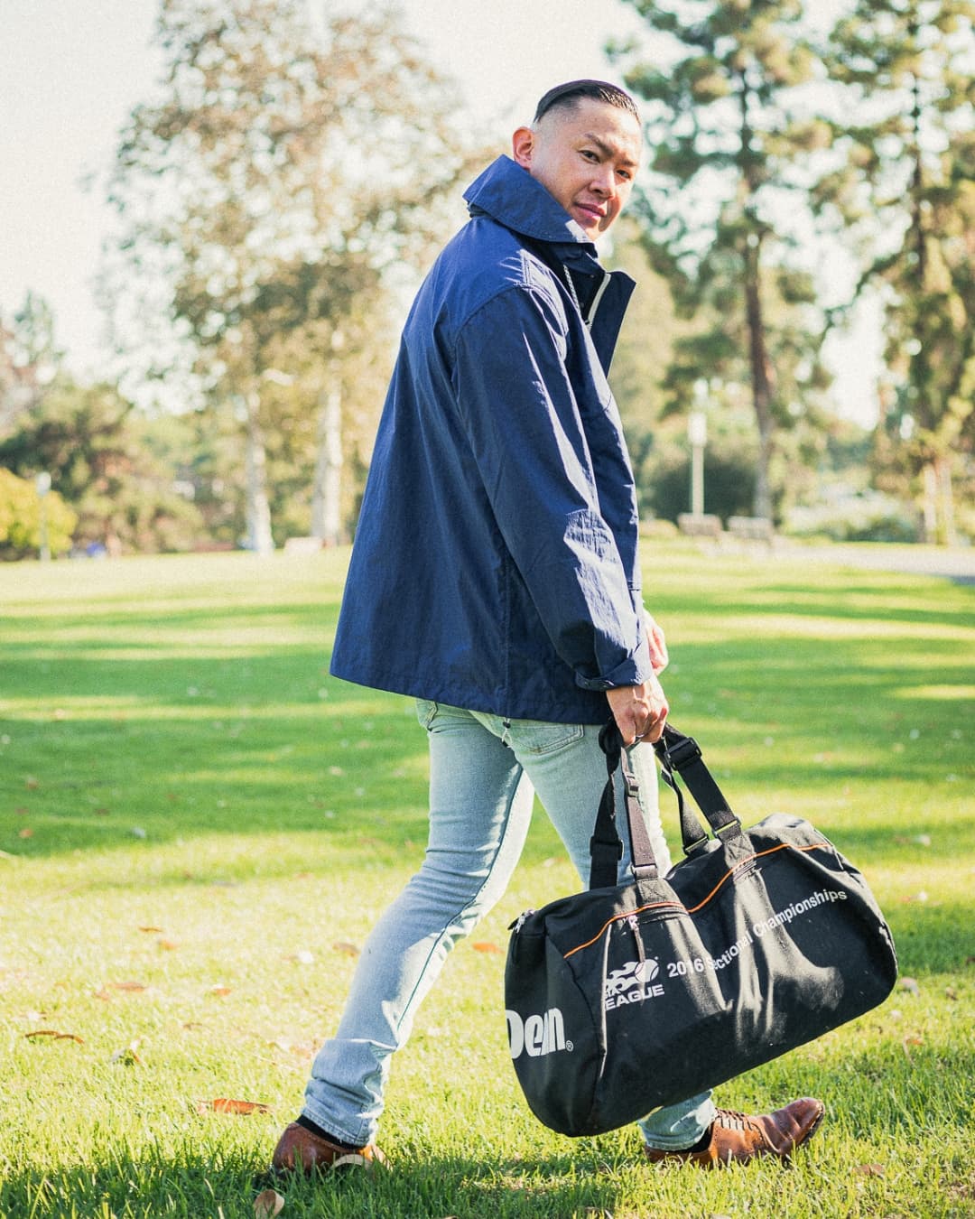 Walking male pose Man posing in windbreaker while walking with a bag.