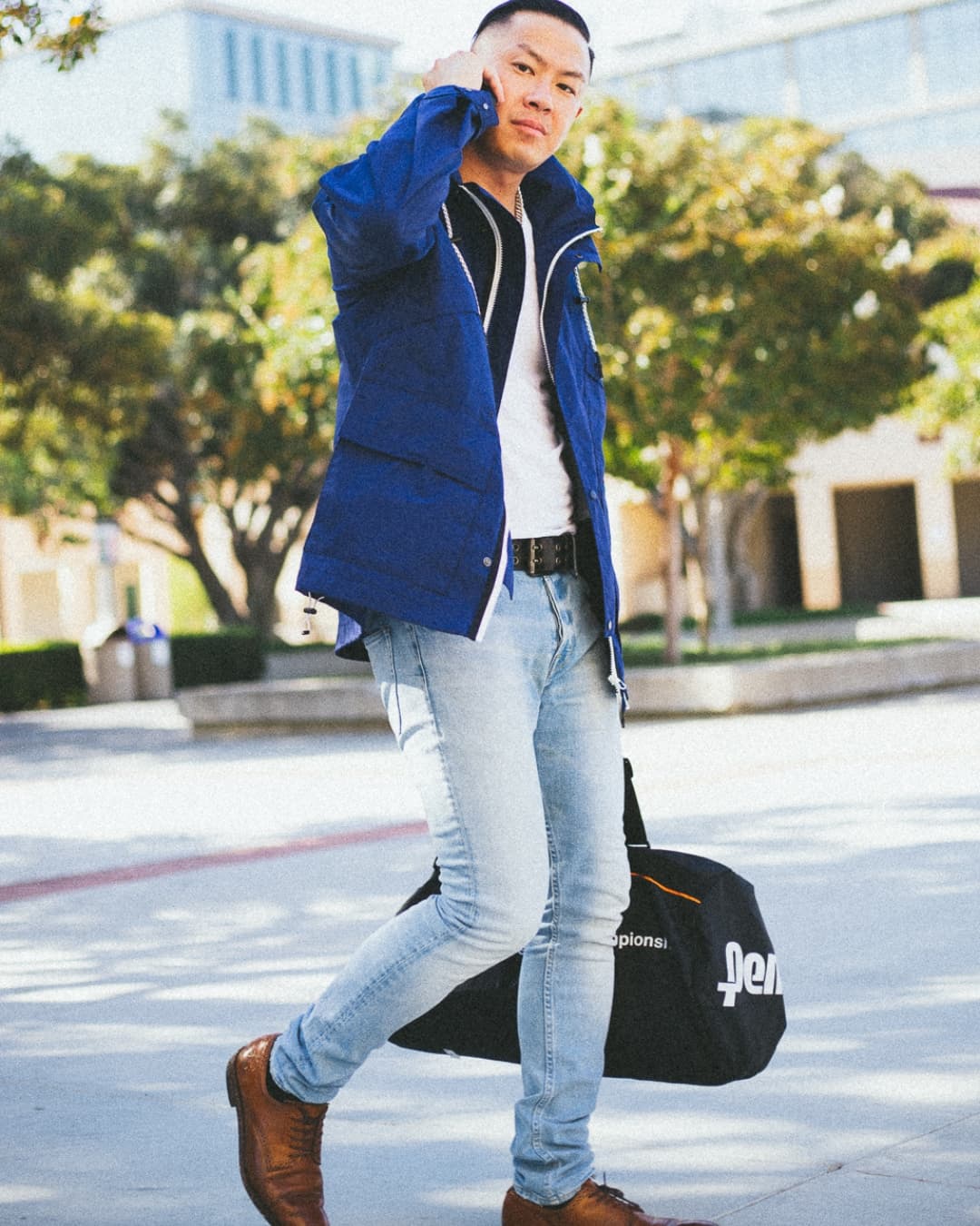 Walking on phone pose Man posing in windbreaker while walking on phone with a bag.
